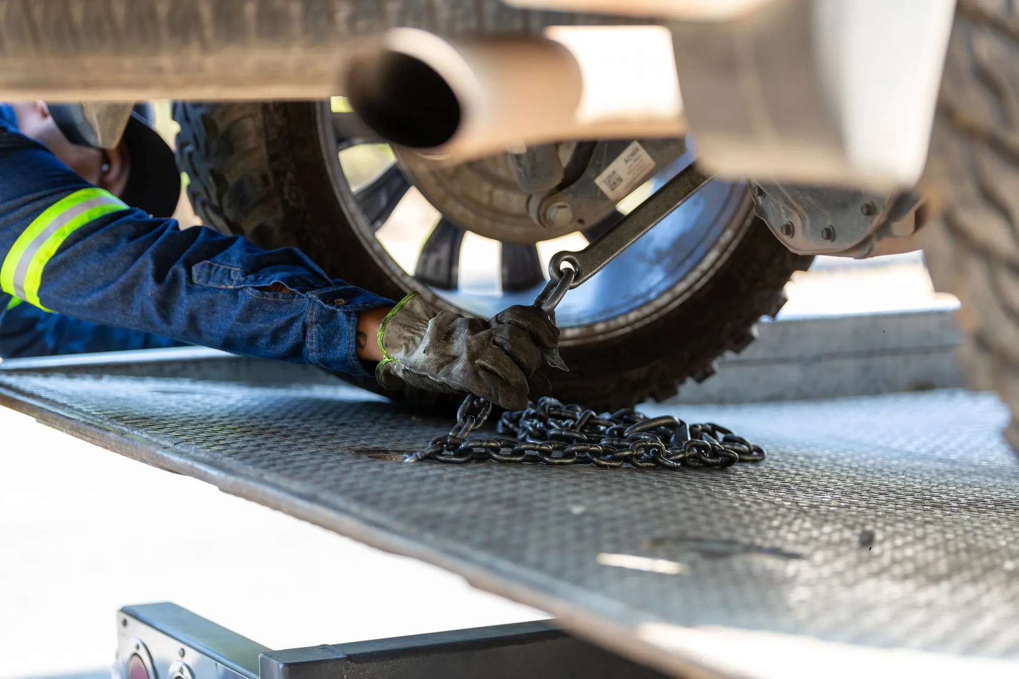 Tow operator in work gloves securing a wheel strap and chain on a flatbed deck